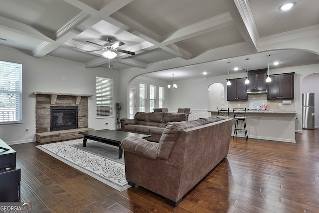 living room featuring ornamental molding, beam ceiling, dark wood-type flooring, a fireplace, and ceiling fan with notable chandelier