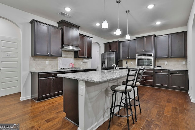 kitchen featuring pendant lighting, an island with sink, appliances with stainless steel finishes, dark hardwood / wood-style floors, and a kitchen breakfast bar