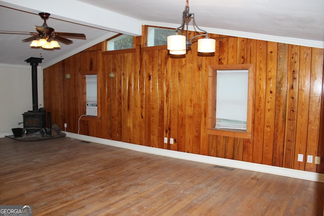 unfurnished living room with hardwood / wood-style flooring, wood walls, a wood stove, and ornamental molding