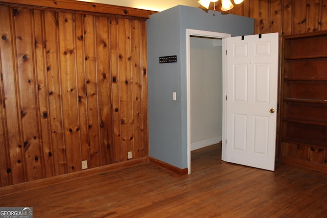 unfurnished room with wood walls and dark wood-type flooring