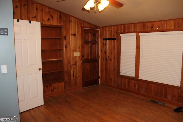 empty room with vaulted ceiling, ceiling fan, dark wood-type flooring, built in features, and wood walls