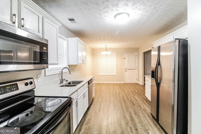 kitchen with white cabinets, hanging light fixtures, sink, appliances with stainless steel finishes, and light hardwood / wood-style floors