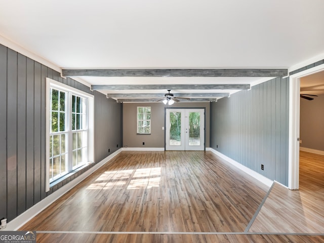 unfurnished room featuring wood-type flooring, wooden walls, beam ceiling, and a wealth of natural light