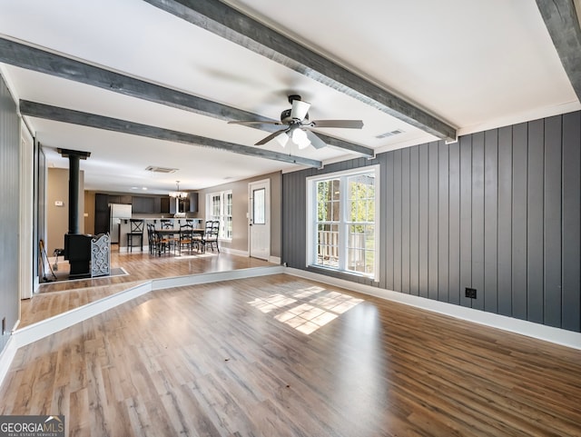 interior space featuring light wood-type flooring, wood walls, beam ceiling, and a wood stove