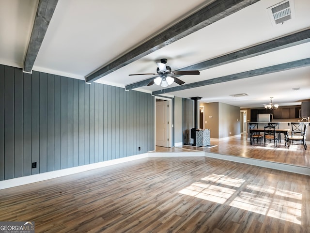 unfurnished living room featuring a wood stove, wooden walls, beam ceiling, and light hardwood / wood-style flooring