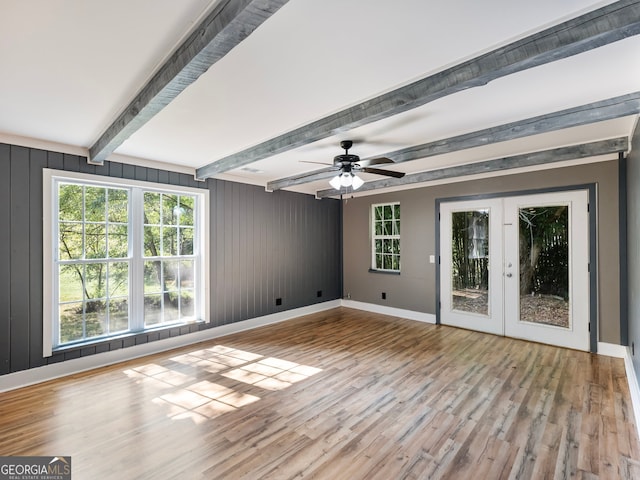 unfurnished room featuring french doors, beamed ceiling, light wood-type flooring, and plenty of natural light