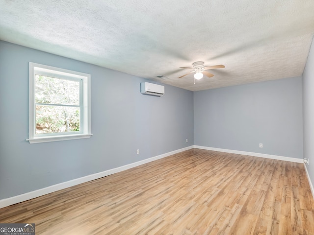 empty room featuring ceiling fan, a textured ceiling, light hardwood / wood-style floors, and an AC wall unit