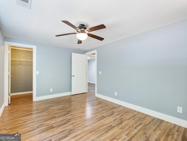 unfurnished bedroom with a closet, a walk in closet, light wood-type flooring, and ceiling fan