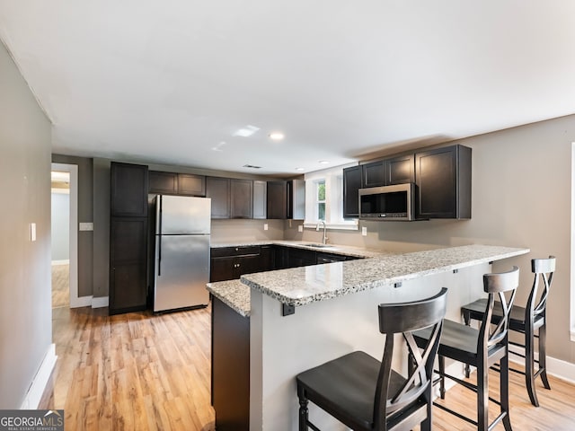 kitchen featuring light wood-type flooring, sink, kitchen peninsula, stainless steel appliances, and light stone countertops