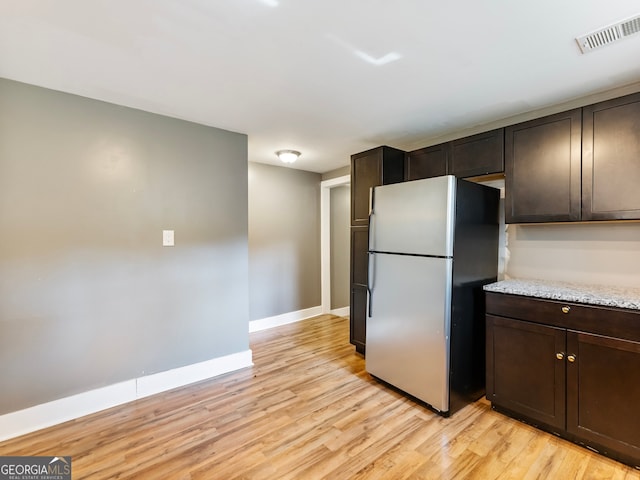 kitchen with stainless steel fridge, dark brown cabinets, light stone countertops, and light hardwood / wood-style flooring