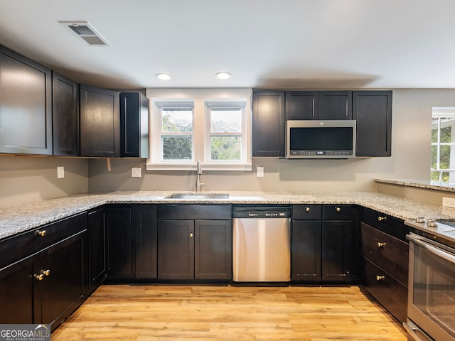 kitchen featuring appliances with stainless steel finishes, light stone countertops, sink, and light hardwood / wood-style floors