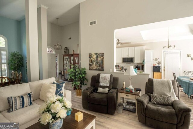 living room with ceiling fan, light hardwood / wood-style floors, and a high ceiling