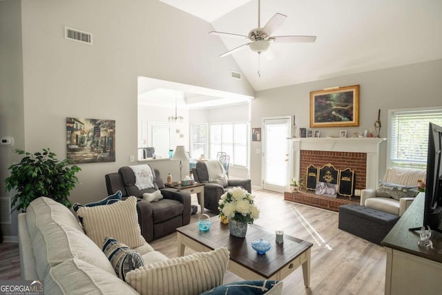 living room featuring a brick fireplace, ceiling fan with notable chandelier, a healthy amount of sunlight, and light hardwood / wood-style flooring