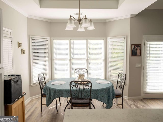 dining space with a raised ceiling, light wood-type flooring, crown molding, and an inviting chandelier