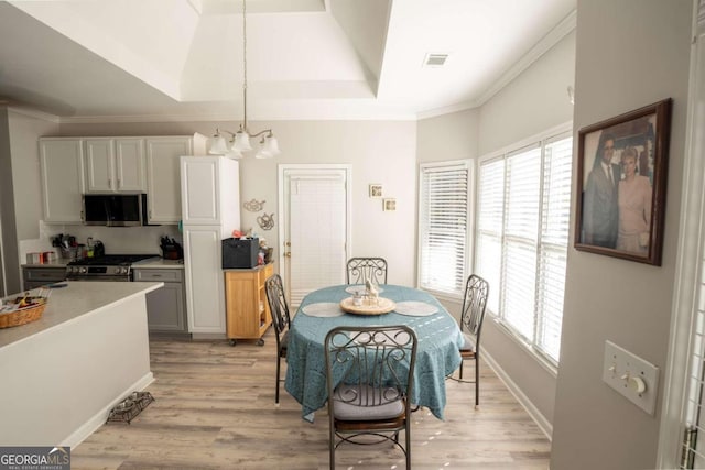 dining area with a notable chandelier, a raised ceiling, plenty of natural light, and light wood-type flooring