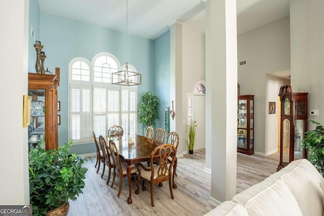 dining room with light hardwood / wood-style floors, a high ceiling, and an inviting chandelier