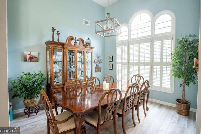 dining room featuring a notable chandelier, light hardwood / wood-style floors, and a towering ceiling