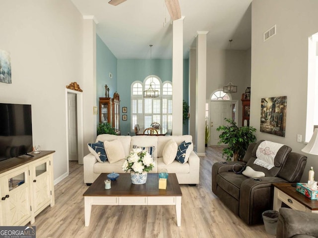 living room with ceiling fan, light wood-type flooring, and a towering ceiling