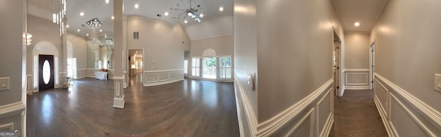 hall featuring a notable chandelier, a towering ceiling, and dark wood-type flooring