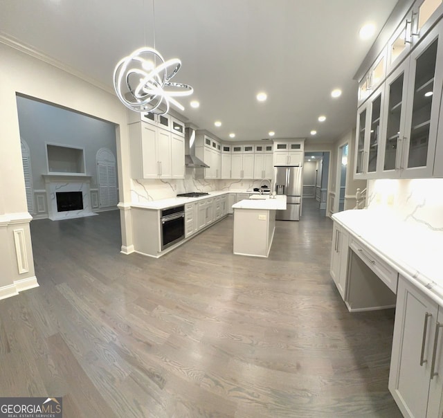 kitchen with decorative light fixtures, wall chimney exhaust hood, appliances with stainless steel finishes, a center island, and dark hardwood / wood-style flooring