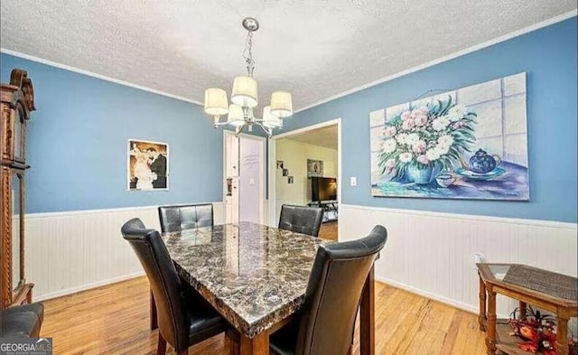 dining room featuring light wood-type flooring, a textured ceiling, ornamental molding, and an inviting chandelier