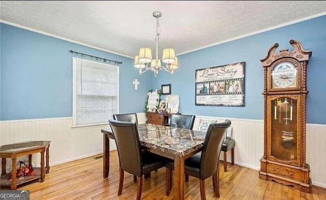 dining space with light hardwood / wood-style floors, ornamental molding, and a chandelier