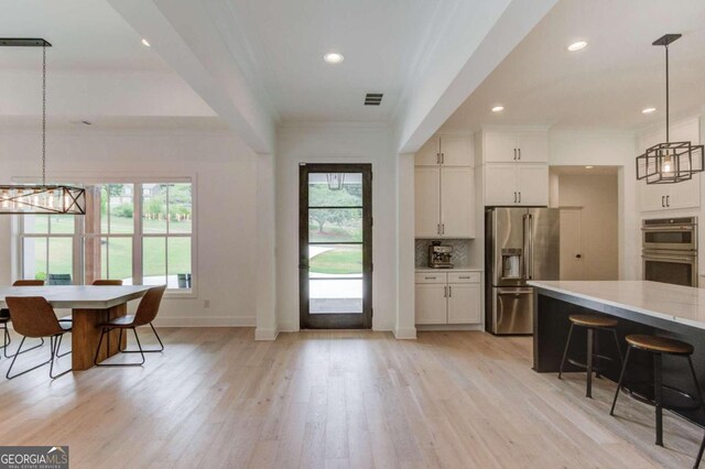 kitchen with appliances with stainless steel finishes, hanging light fixtures, light hardwood / wood-style floors, and white cabinets