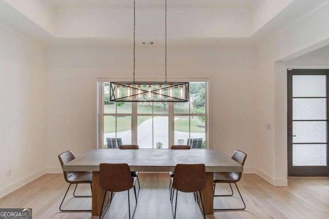 dining area featuring a notable chandelier, light hardwood / wood-style floors, and a raised ceiling