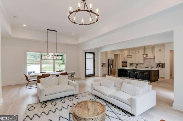 living room with light hardwood / wood-style flooring, a chandelier, a tray ceiling, and sink