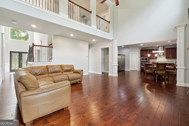 living room featuring french doors, decorative columns, a towering ceiling, and dark wood-type flooring