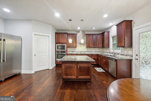 kitchen featuring a center island, dark wood-type flooring, wall chimney range hood, stainless steel appliances, and decorative light fixtures