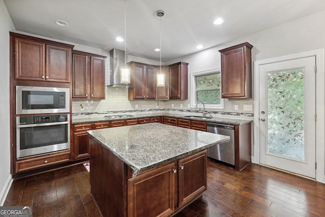 kitchen with hanging light fixtures, wall chimney range hood, stainless steel appliances, a center island, and dark hardwood / wood-style flooring