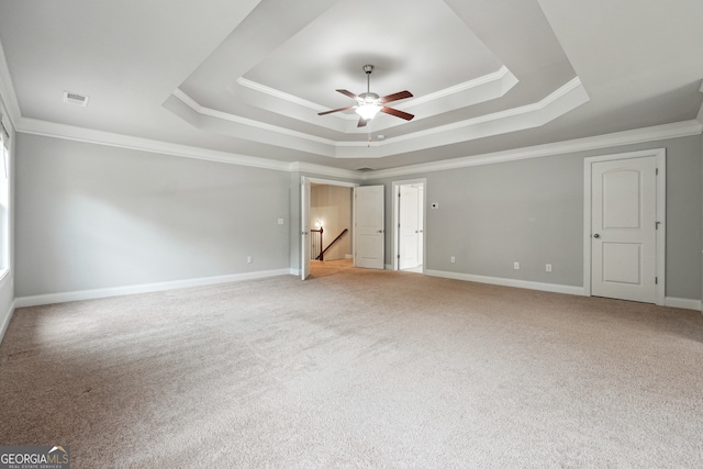 empty room with a raised ceiling, ceiling fan, light colored carpet, and crown molding