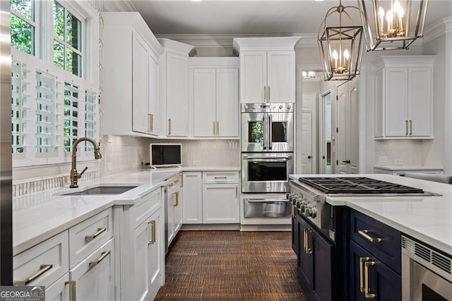 kitchen with appliances with stainless steel finishes, sink, blue cabinets, white cabinetry, and pendant lighting