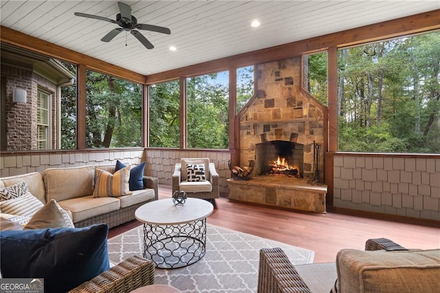 sunroom / solarium featuring a stone fireplace, wood ceiling, and ceiling fan