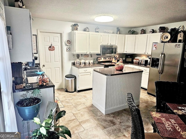 kitchen with a textured ceiling, stainless steel appliances, sink, white cabinets, and a center island