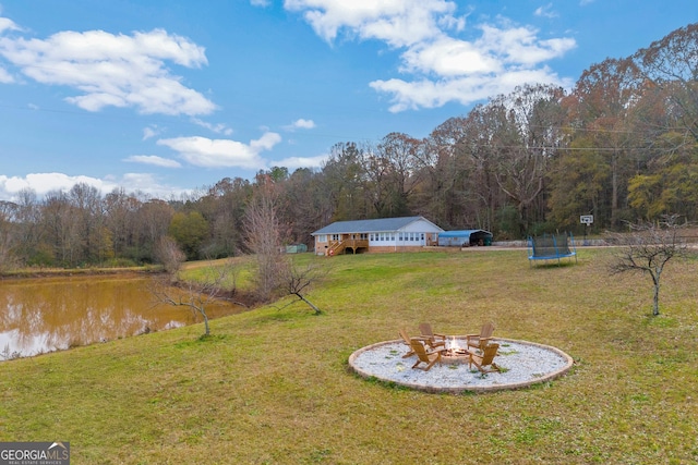 view of yard featuring a water view, a fire pit, and a trampoline