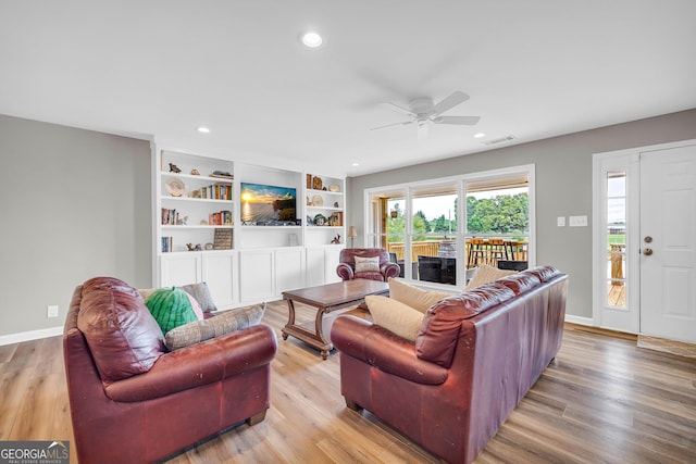 living room with ceiling fan, light wood-type flooring, and built in shelves