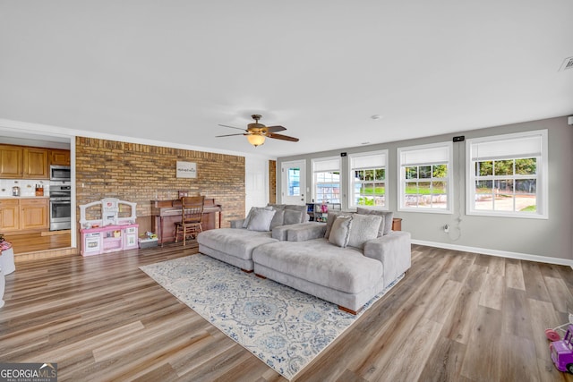 living room with ceiling fan, light hardwood / wood-style flooring, and brick wall