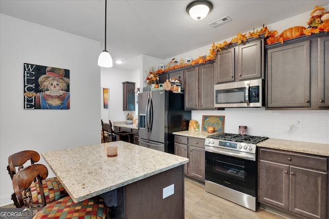 kitchen featuring light hardwood / wood-style floors, hanging light fixtures, a kitchen breakfast bar, appliances with stainless steel finishes, and dark brown cabinetry