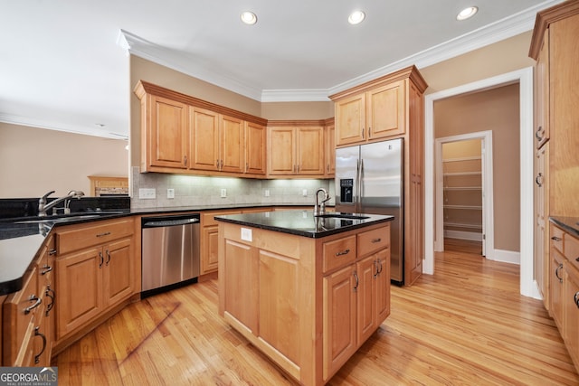 kitchen featuring light wood-type flooring, tasteful backsplash, an island with sink, appliances with stainless steel finishes, and crown molding