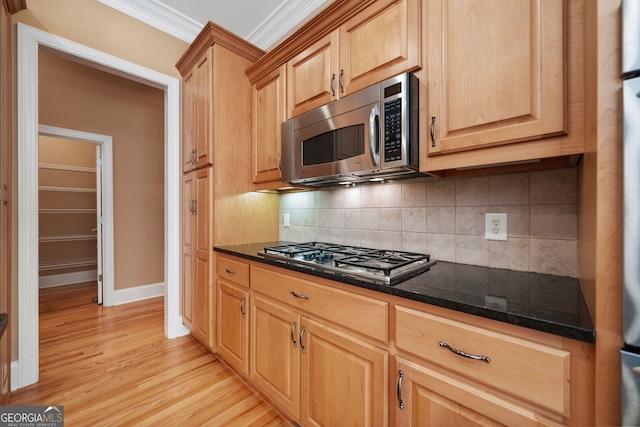 kitchen featuring ornamental molding, backsplash, dark stone counters, stainless steel appliances, and light wood-type flooring