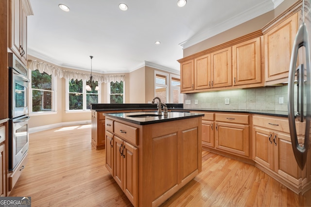 kitchen featuring an island with sink, sink, decorative light fixtures, crown molding, and light hardwood / wood-style floors