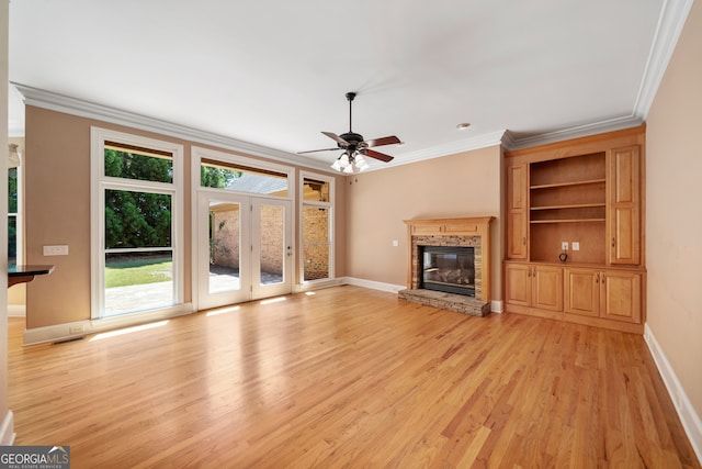 unfurnished living room featuring light hardwood / wood-style floors, crown molding, ceiling fan, and a stone fireplace