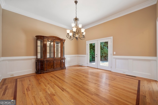 unfurnished dining area featuring a notable chandelier, light hardwood / wood-style floors, french doors, and crown molding