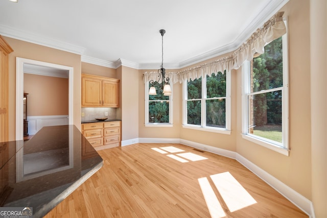 unfurnished dining area featuring light wood-type flooring, crown molding, and a chandelier