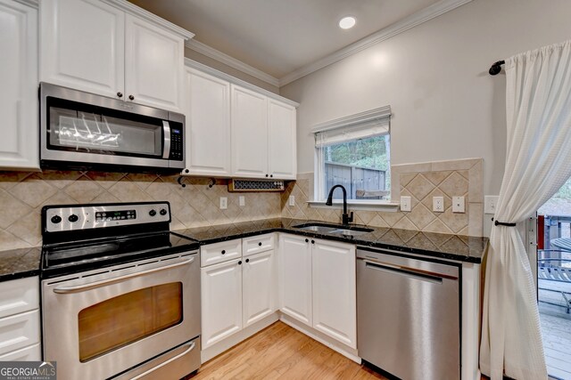 kitchen featuring tasteful backsplash, sink, white cabinets, light hardwood / wood-style flooring, and stainless steel appliances