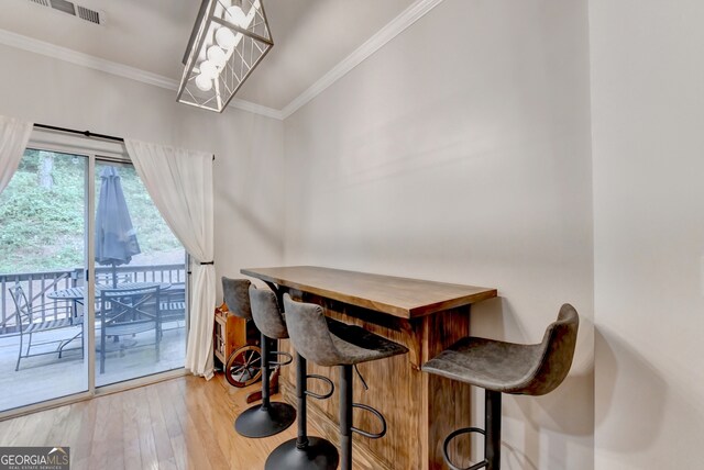 dining space featuring ornamental molding, indoor bar, and light hardwood / wood-style floors