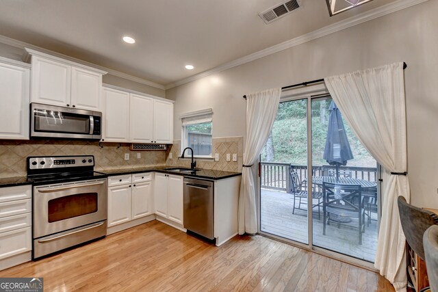 kitchen with white cabinets, sink, backsplash, stainless steel appliances, and light wood-type flooring