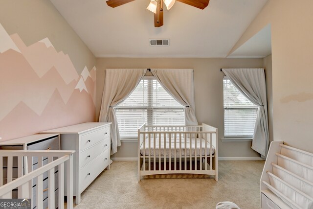 bedroom with ceiling fan, a nursery area, and light carpet